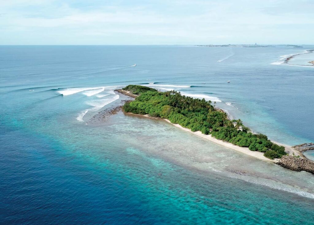 olas perfectas rompiendo alrededor de una isla en maldivas con reef y agua cristalina.