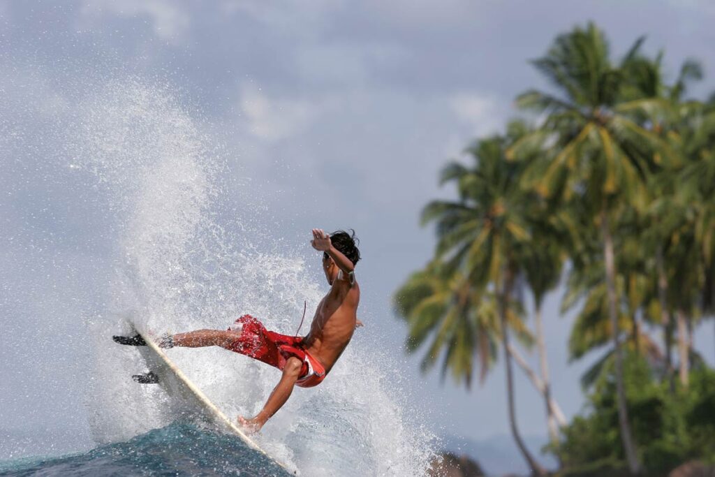 surfista local haciendo un giro en una ola tropical de Indonesia con palmeras al fondo